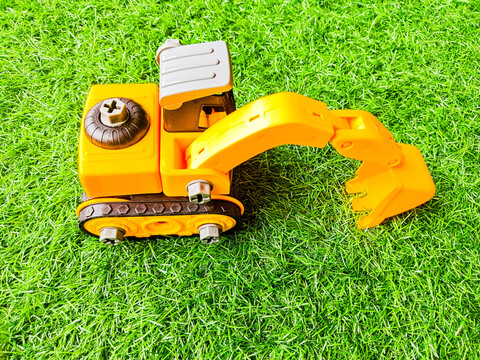 Yellow toy excavator on green artificial grass background, take apart construction vehicle toy for kids development.