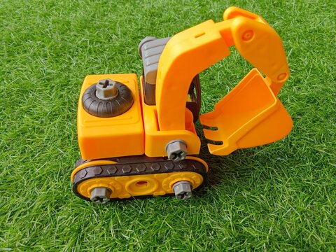 Yellow toy excavator on green artificial grass background, take apart construction vehicle toy for kids development.
