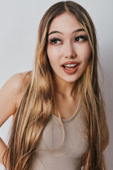 Naklejka premium Young woman with long blonde hair and casual clothing looking to side with expression for surprise and curiosity on neutral background in studio lighting indoors.