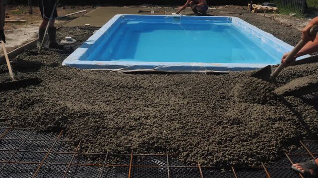 Workers are leveling cement and preparing foundation for swimming pool with metal rebar grid.