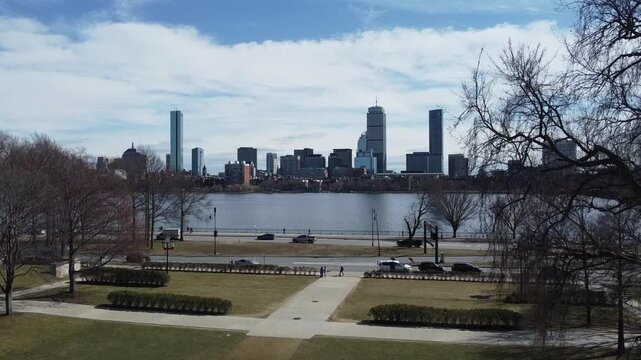 Aerial drone view rising above Memorial Drive near MIT in Cambridge, Massachusetts, revealing the Boston skyline and the Charles River at sunset.
