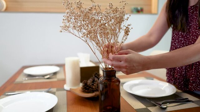 Asian Woman Arranging Dried Flowers in a Brown Glass Vase