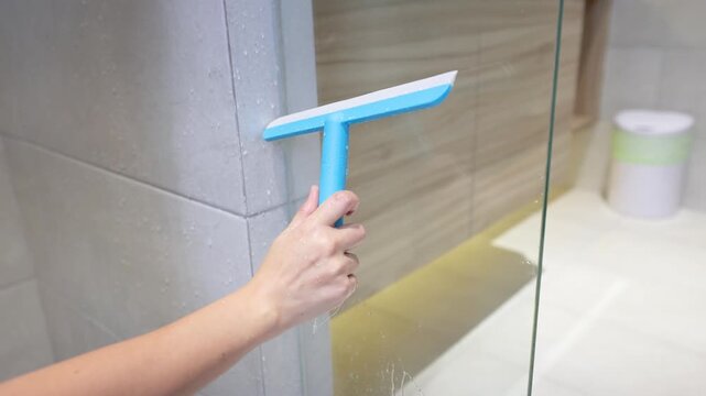 Person Cleaning Bathroom Glass Shower Door with Blue Squeegee Tool