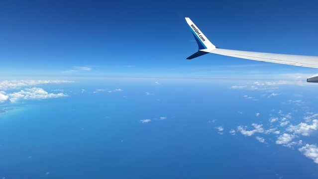 Plane flying into blue sky seen over wing.
