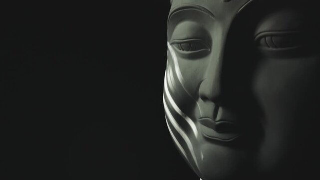 The face of the Buddha statue in the darkness is illuminated by a flickering light