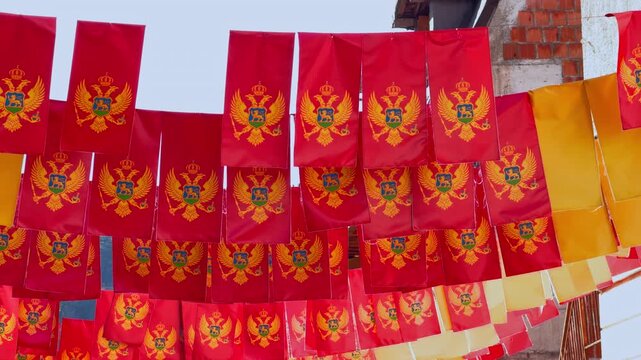Row of Montenegro national flag bunting with double headed eagle crest hanging across street in sunny day, balkan patriotic celebration decoration