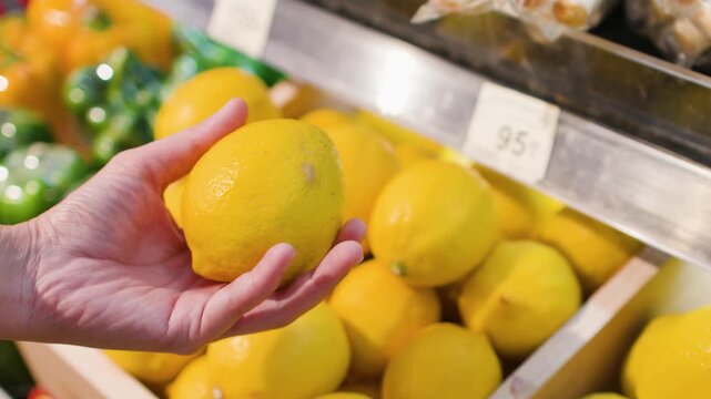Asian Person Hand Picking Fresh Lemons in a Supermarket Grocery Store