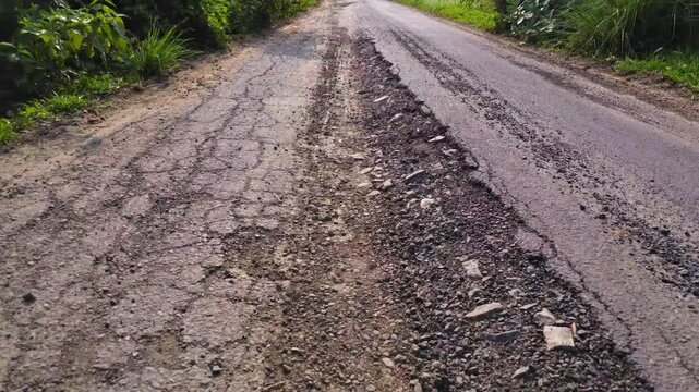 Damaged Asphalt Road with Potholes in Rural India Transportation Infrastructure Close Up. Rural Indian Road with Broken Asphalt Surface and Deep Cracks Slow Motion. Cracks and Road Potholes Outdoors.
