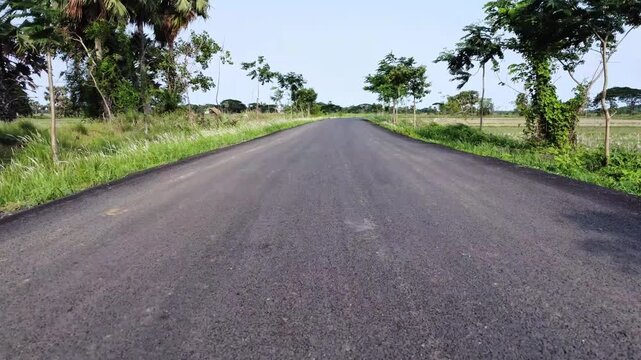 Low angle shot of an empty indian asphalt road stretching into the rural countryside. Indian road running through village farmlands. 
