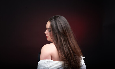 Naklejka premium A young woman poses in a white lace blouse on a dark blue background. The shirt is unbuttoned and her beautiful breasts are visible.