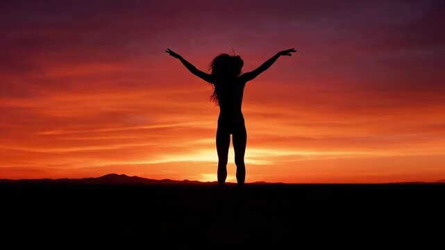 A woman stands in a serene landscape with arms outstretched towards a vibrant orange and red sunset