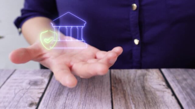 Secure and validated banking. Close-up of a woman's hand at a table holding a virtual bank icon with a shield and a checkmark.
