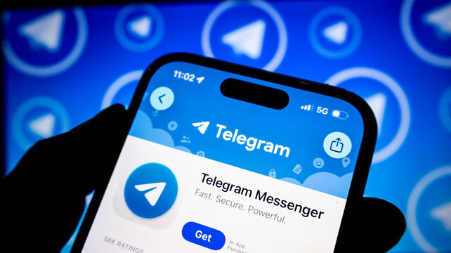 Closeup of a hand holding a smartphone displaying the telegram messenger app store page with the app logo and download button