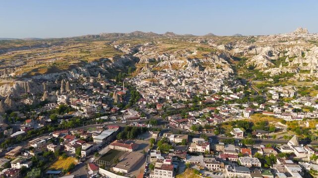 Goreme, Nevsehir, Turkey. Aerial view of the town nestled within eroded valleys and fairy chimney rock formations of Cappadocia, bathed in warm morning light under a clear blue sky.. Aerial View, Dep
