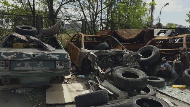 Destroyed And Burnt Cars In Junkyard. Car Cemetery Full Of Damaged Autos And Old Used Tires. Environmental Pollution