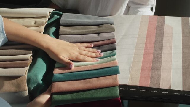 Customer selects fabric swatches from stack with hand touching soft texture for interior design choice.