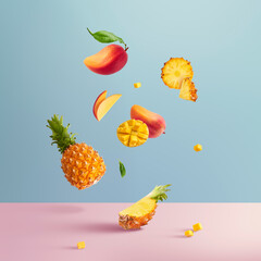 Fototapeta premium Levitating fresh tropical fruits. Sliced and whole pineapple and mango falling in the air on blue and pink background. Creative dynamic summer food composition.