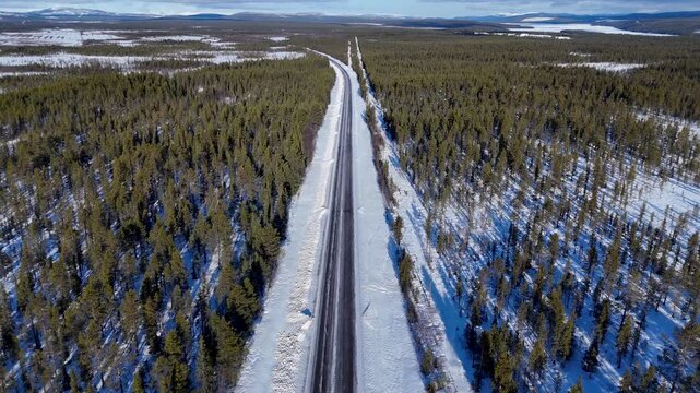 Beautiful Aerial View of a Snowy Straight and curve Highway through Endless Arctic Pine Forest in Sweden, 4K 60fs Horizontal Forward Drone Shot following two cars on a sunny winter day, leading lines