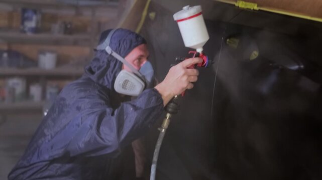 Auto body painter spraying lacquer in close-up on masked black car panel, applying clear coat during final refinishing after collision repair, insurance claim service and paint restoration.