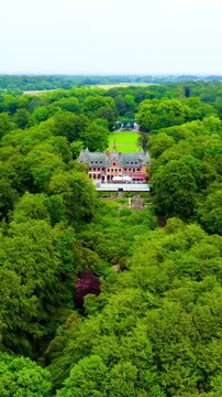 Vertical video. Sweden. Sofiero Palace, Dutch Renaissance red-brick castle rising from dense green parkland, aerial pullback revealing sweeping lawns and the Oresund Strait under overcast summer skie