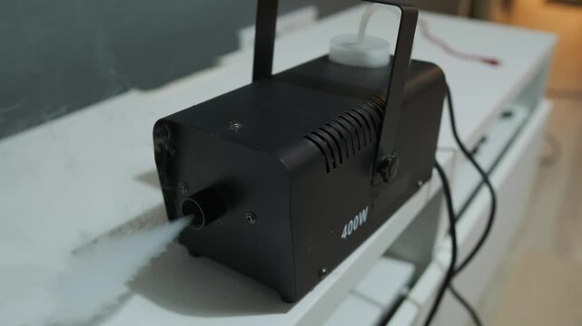 Compact smoke machine releasing theatrical fog indoors, professional stage equipment creating dense smoke effect for party lighting, concerts, filming and special events.