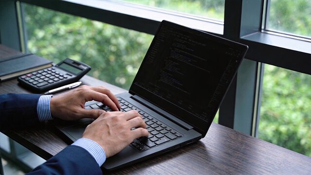 Programmer typing code on laptop in modern office, software development and web programming workflow for tech professionals and IT specialists working remotely.