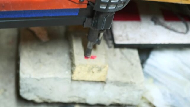Electric nail gun driving fastener into wooden block in close-up, professional construction equipment for carpentry, woodworking and industrial assembly work.
