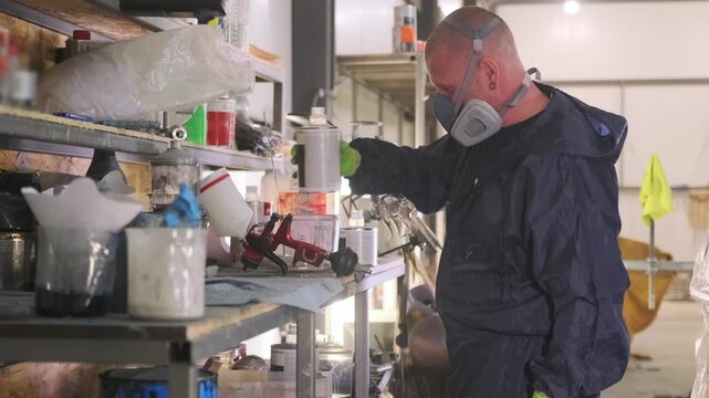 Auto body painter pouring clear coat mixture into spray cup at workshop shelf, preparing lacquer ingredients for vehicle finishing after paintwork, insurance repair and collision refinishing service.
