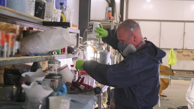Auto body painter mixing lacquer ingredients for car clear coat after painting, preparing materials at workshop shelf for vehicle refinishing, repair and final finishing.
