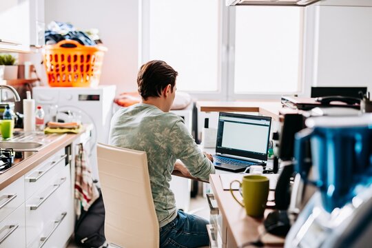 Man working from home kitchen with laptop and coffee mug