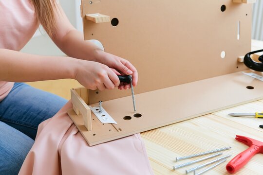 Woman assembling wooden furniture with screwdriver at home