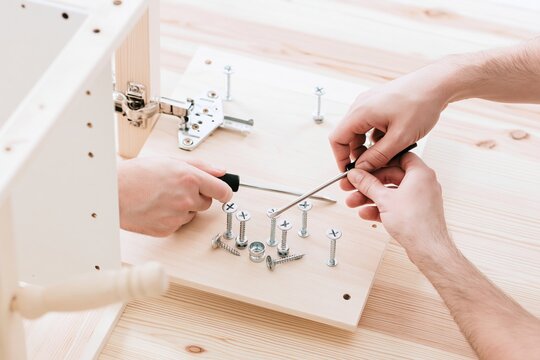 Hands assembling cabinet with screws and screwdriver