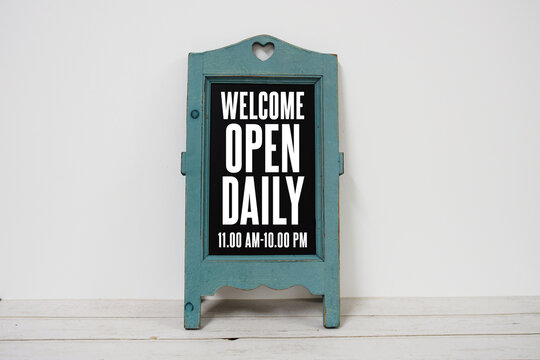 Wooden blackboard easel with text "Welcome Open Daily 11am - 10pm" on wooden background