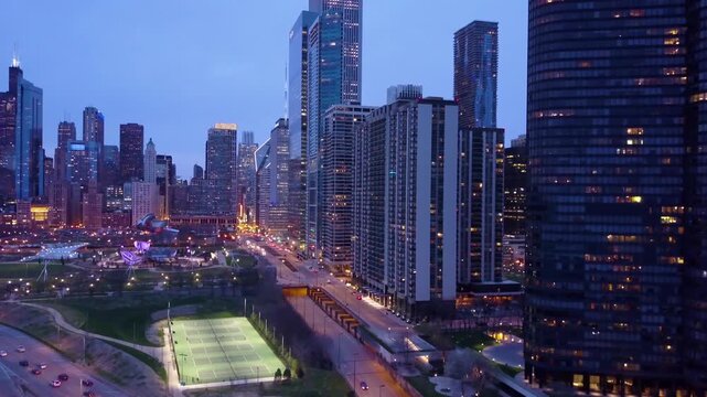 Aerial view of Chicago skyline and Maggie Daley park at twilight with city lights and street traffic.