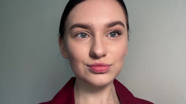 Young woman applying mascara, showing daily beauty routine, demonstrating facial makeup, highlighting smooth foundation, natural concealer, defined cheekbones, subtle nose contour, glowing lips.