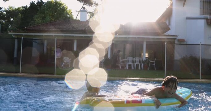 Boy sprinting and diving into backyard pool with explosive splash as water droplets hit camera lens, while another boy floats calmly on inflatable mattress nearby