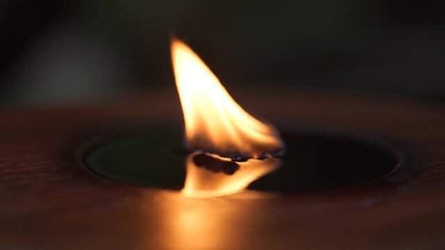 A small flame burns in darkness.