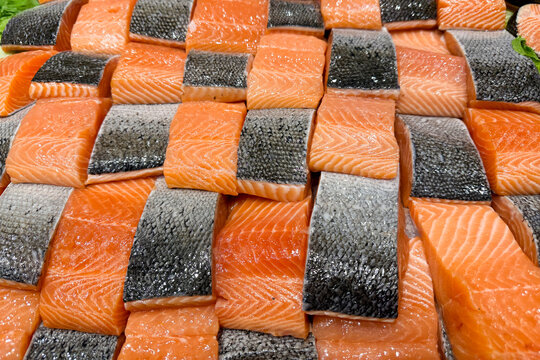 Neatly arranged fresh salmon fillets with skin on display at a fish market.