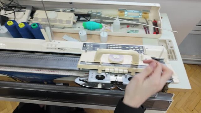 Top down view of a knitting workstation, including multiple spools of yarn, thread guides, and machine controls