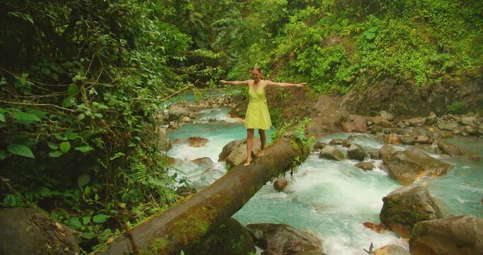 Tourist balancing on fallen log above vibrant Blue Falls river in Costa Rica scenery