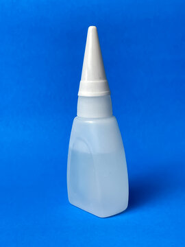 A small plastic bottle with a white dispenser cap for superglue or other liquid adhesives. Close-up of the isolated object against a blue background.