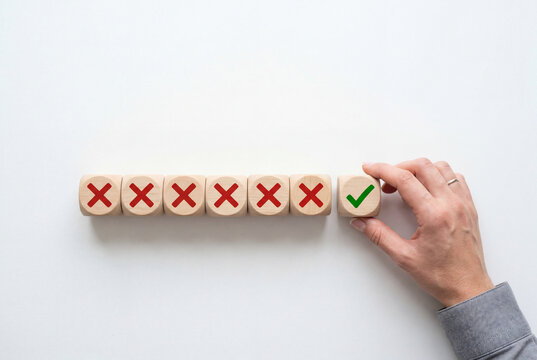 Hand placing wooden cube with green checkmark next to red crosses