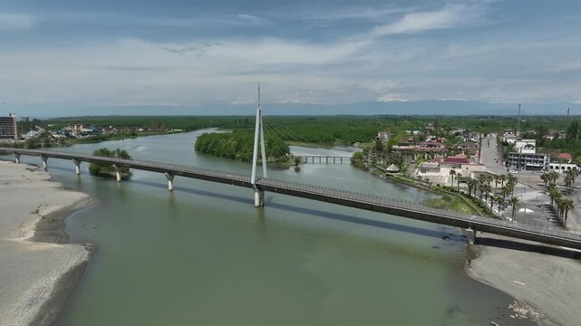 Aerial view of Anaklia resort in Georgia featuring the futuristic observation tower, pedestrian bridge over Enguri river, sandy beach, and Black Sea coastline on a sunny day.