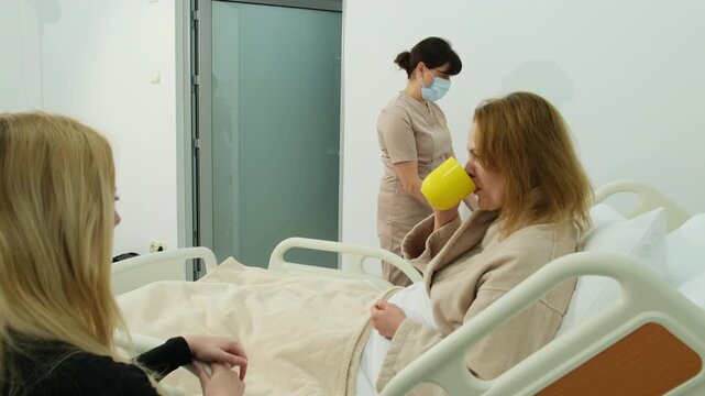 Woman patient warmly hugs visiting relative to say goodbye. Nurse carefully brings essential medicines on small rolling cart. Slow motion