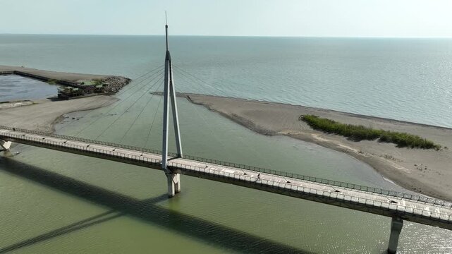 Aerial view of Anaklia resort in Georgia featuring the futuristic observation tower, pedestrian bridge over Enguri river, sandy beach, and Black Sea coastline on a sunny day.