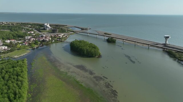 Aerial view of Anaklia resort in Georgia featuring the futuristic observation tower, pedestrian bridge over Enguri river, sandy beach, and Black Sea coastline on a sunny day.