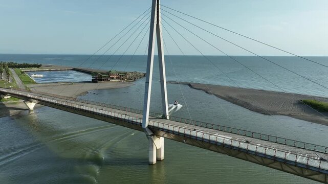 Aerial view of Anaklia resort in Georgia featuring the futuristic observation tower, pedestrian bridge over Enguri river, sandy beach, and Black Sea coastline on a sunny day.