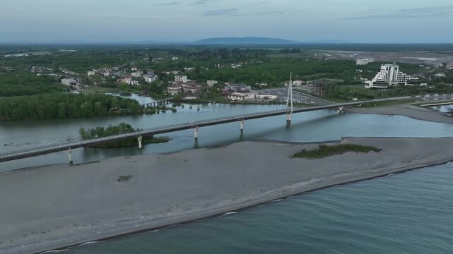 Aerial view of Anaklia resort in Georgia featuring the futuristic observation tower, pedestrian bridge over Enguri river, sandy beach, and Black Sea coastline on a sunny day.