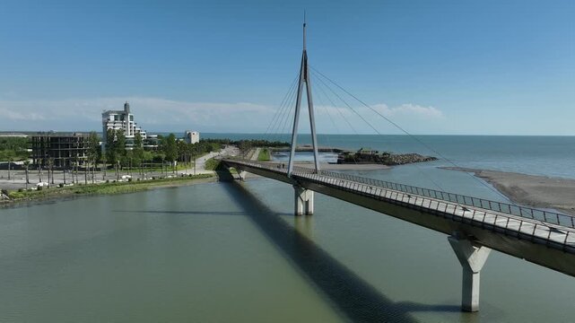 Aerial view of Anaklia resort in Georgia featuring the futuristic observation tower, pedestrian bridge over Enguri river, sandy beach, and Black Sea coastline on a sunny day.