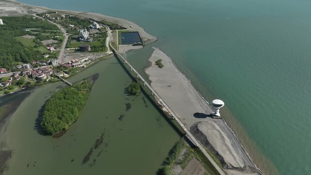 Aerial view of Anaklia resort in Georgia featuring the futuristic observation tower, pedestrian bridge over Enguri river, sandy beach, and Black Sea coastline on a sunny day.
